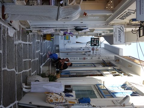 Whitewashed alley with shops, signs and tourists sitting in the shade, Mykonos