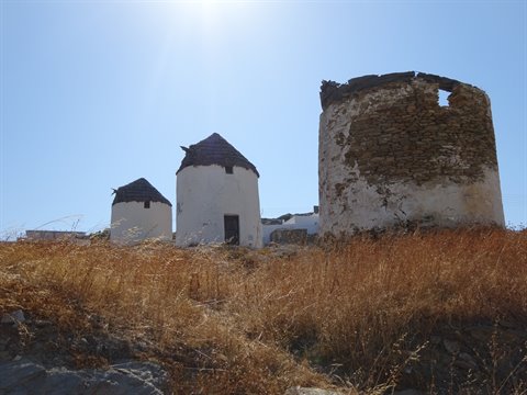 Old white stone windmills under bright sun among dry grass