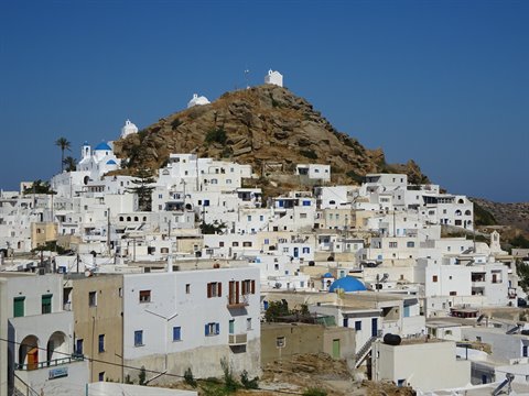 White houses below rocky hill, blue domes, clear sky, Ios