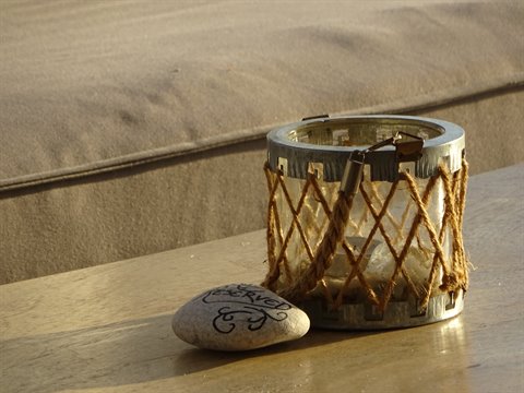 Glass candle holder with rope and engraved stones on wooden table, warm light