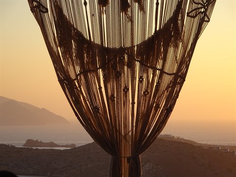 Macramé rope curtain against golden sky with sea and hills behind