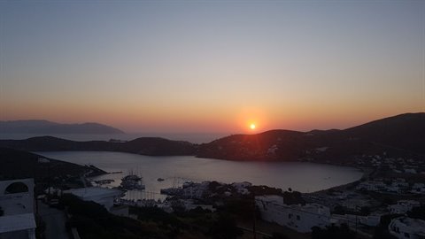 Low sun over bay with marina, dark hills and white houses, orange sky