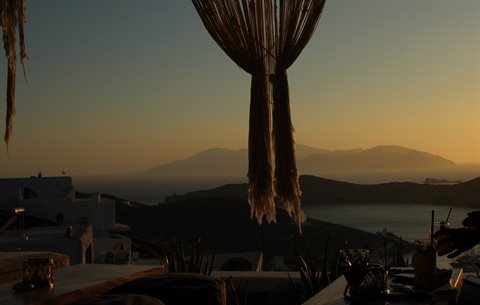 Rope curtain over terrace at dusk, islands on the sea, drinks on table
