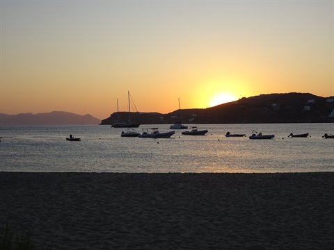 Boats anchored in a bay at sunset, sandy beach in the foreground