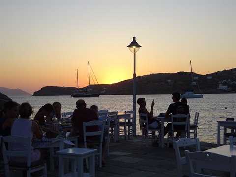 People seated at taverna tables by the harbor at dusk