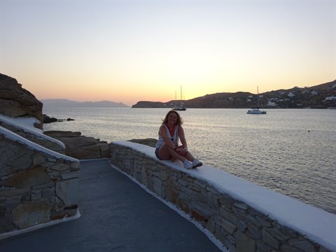 Woman sitting on stone wall by the sea with boats, warm light