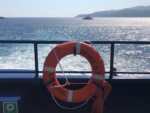 Orange lifebuoy aboard Sifnos Jet ferry, white wake across Aegean hills