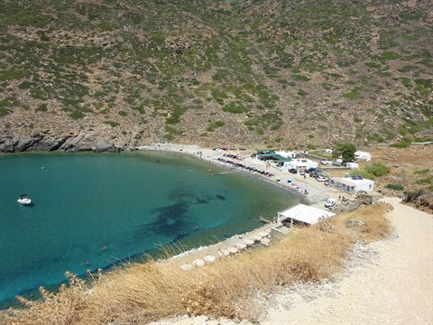 Sandy beach with umbrellas and a boat in turquoise water below dry hills