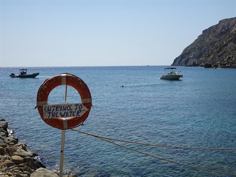 Orange lifebuoy reading Entrance to the Water on rocky shore, boats moored