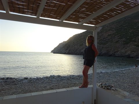 Blonde woman under cane pergola on pebble beach in Sifnos
