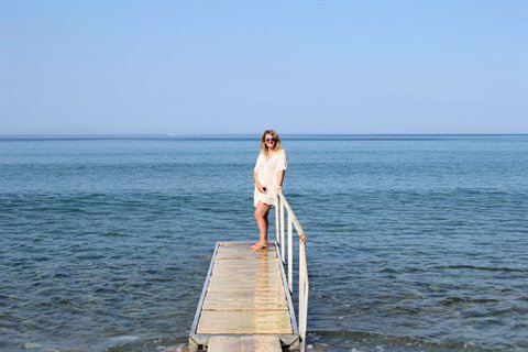 Woman in white dress on wooden pier over blue sea, Sifnos