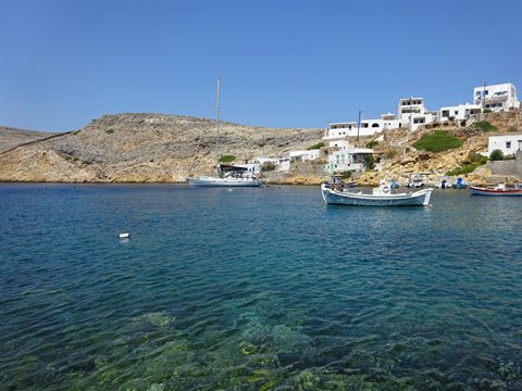 White boat moored in turquoise bay, whitewashed houses on the hill, Sifnos