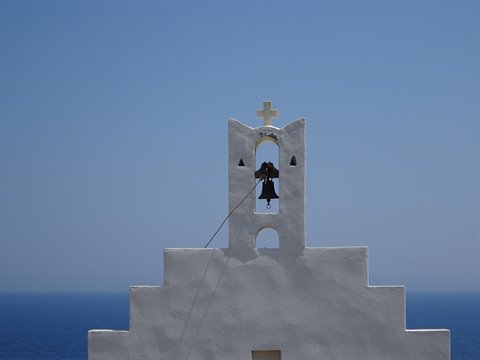 Whitewashed bell tower with bell and cross above the Sifnos sea