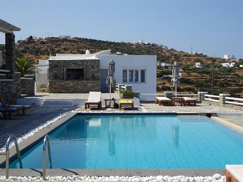 Blue pool with loungers and umbrellas among stone houses in Sifnos