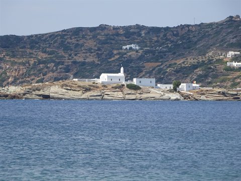 White Chrisopigi monastery on granite rock, blue sea, arid hills behind