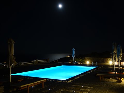Illuminated pool at night under the moon, closed umbrellas, Sifnos