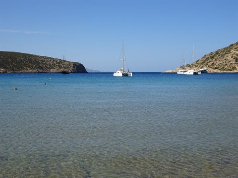 Catamarans and yachts anchored in turquoise bay, arid hills behind