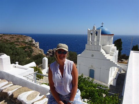 Smiling woman beside a white church with blue dome overlooking the sea, Sifnos