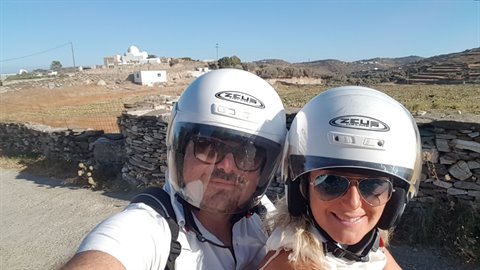 Scooter selfie with white helmets past dry stone walls, church behind