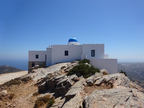 White church with blue dome on Sifnos rocky summit, clear sky