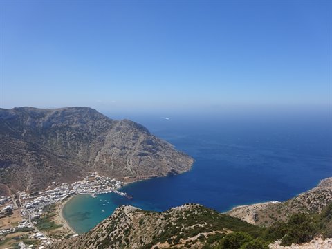 Whitewashed village on a turquoise bay between arid hills under blue sky