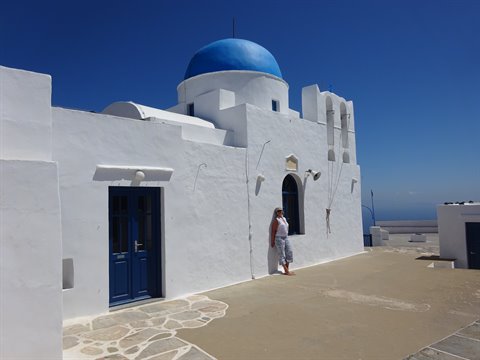 Woman beside whitewashed church with blue dome in Sifnos
