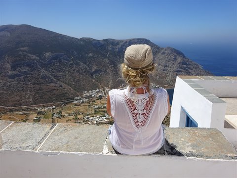 Woman sitting on a stone wall overlooking Sifnos village and sea