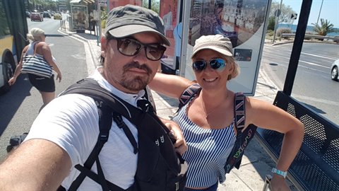 Couple selfie with backpacks at a sunny bus stop