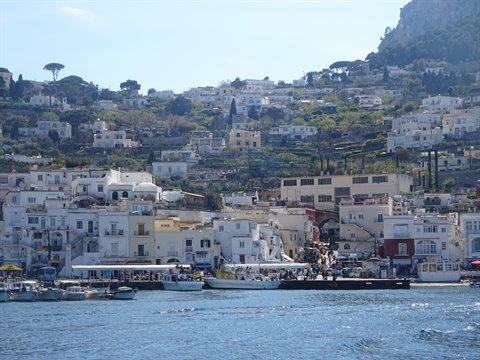 White boats at Capri harbor, colorful houses on the sunny hillside