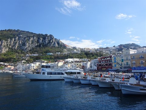 White boats moored at Capri harbor beneath colorful houses and rocky cliffs
