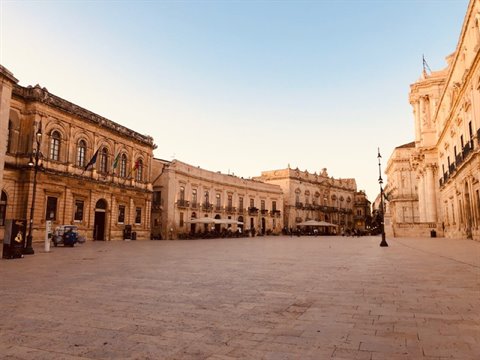 Piazza Duomo in Syracuse, baroque stone buildings under a clear blue sky