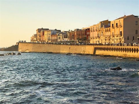 Siracusa seafront on Ortigia island, colorful houses above stone walls at sunset