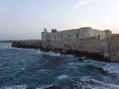 Old stone fortress by the sea, waves crashing against the walls