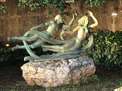 Bronze sculpture of two flying dancers on a rocky boulder, among green bushes