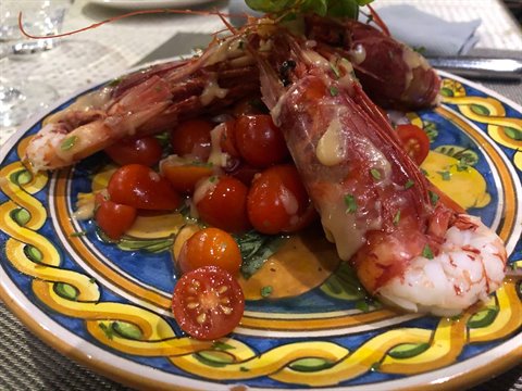 Red prawns with cherry tomatoes on yellow and blue decorated ceramic plate