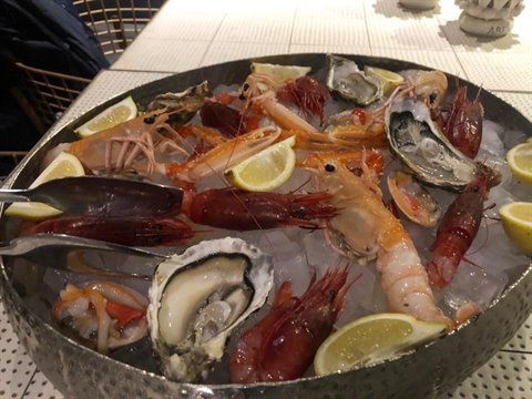 Metal platter with prawns, langoustines and oysters on ice, lemon slices