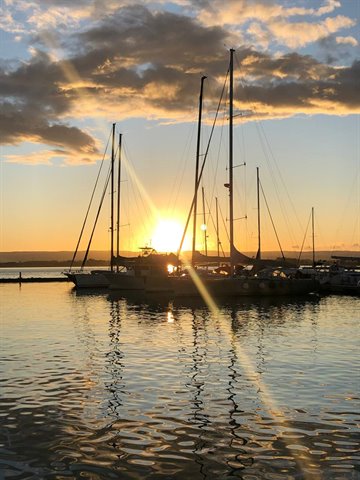 Sailboat masts in the marina, low sun through clouds reflecting on calm water