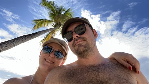 Couple selfie in sunglasses under a leaning palm tree on the beach