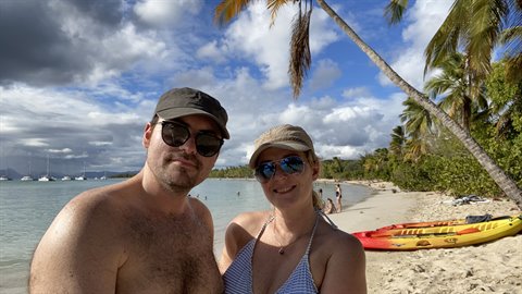 Couple selfie on palm-fringed beach, yellow kayaks and sailboats behind