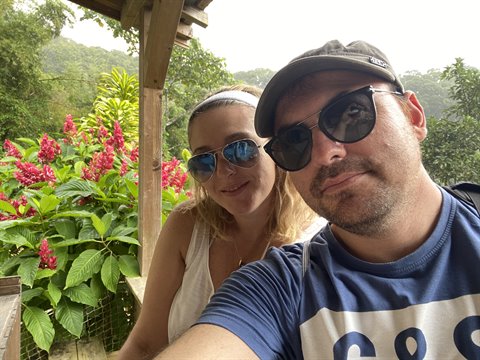 Couple selfie under wooden pergola, tropical red flowers in Martinique