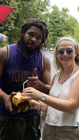 Woman in headband and dreadlocked vendor opening a fresh coconut on Saint-Pierre roadside