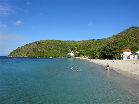 Swimmers in turquoise water on the sandy beach of Anse Dufour, green hills