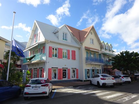 White Creole house with pink shutters in Fort-de-France, parked cars under blue sky