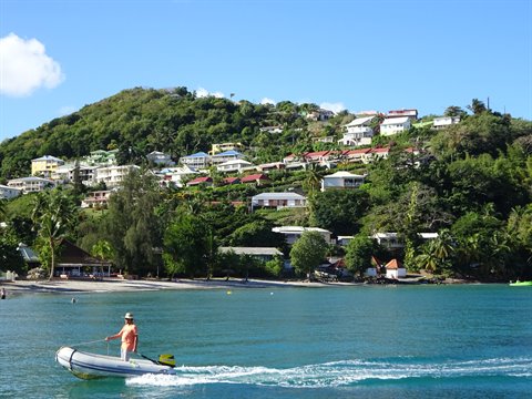 Man on inflatable boat near Les Anses-d'Arlet beach, houses on green hill