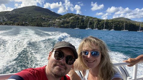 Couple taking selfie on moving boat, white wake and sailboats in Martinique