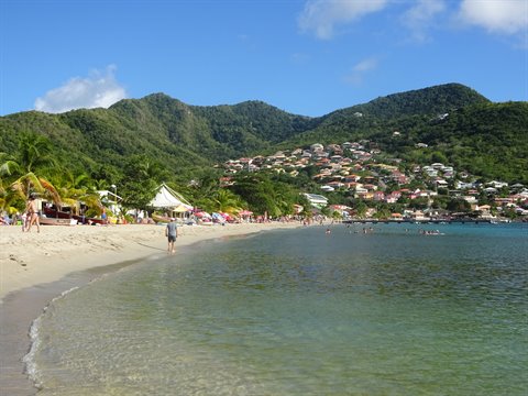 White sand beach at Les Anses-d'Arlet, swimmers and houses beneath green hills