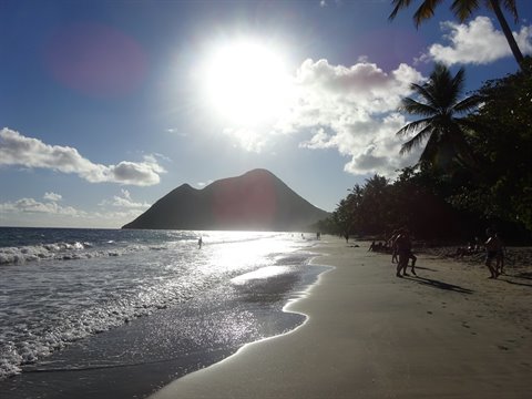 Le Diamant beach, bright sun on wet sand, swimmers by Morne Larcher hill