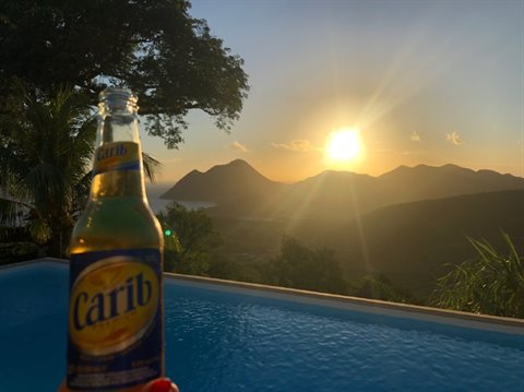 Carib beer bottle by the pool as the low sun glows over the hills
