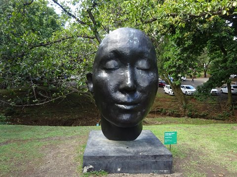Bronze sculpted head on stone base among trees, Fort-de-France