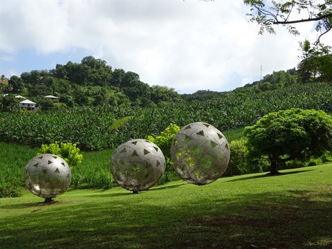 Metal spheres among green banana fields under white clouds, tropical garden in Martinique